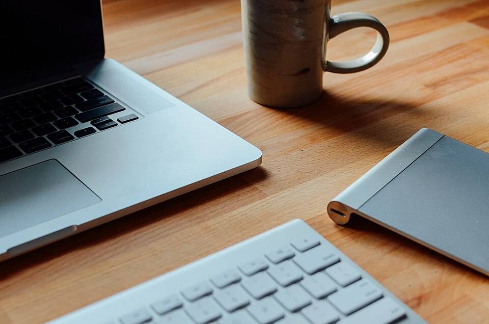 Laptop dan cangkir kopi di meja kerja, melambangkan kebiasaan membaca panduan